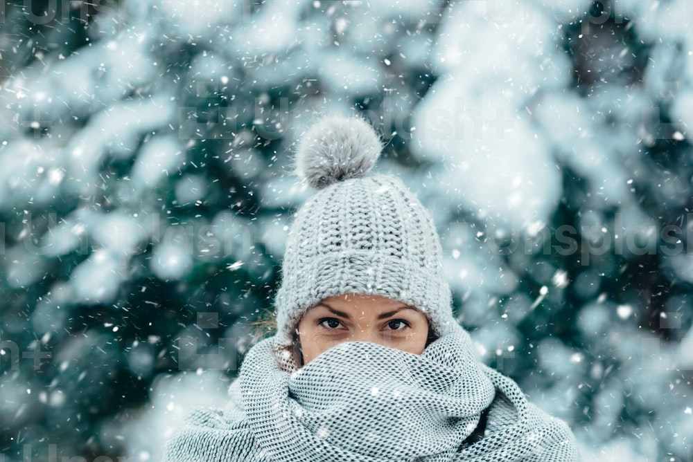 在寒冷的冬日，一位美丽的年轻女子在雪天中戴着围巾和帽子的画像